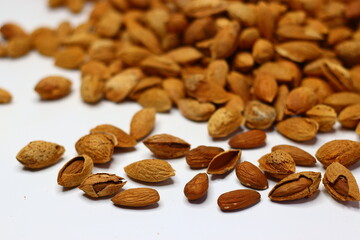 Raw almonds with shells scattered on a white surface, showcasing their natural texture