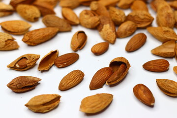 Raw almonds with shells scattered on a white surface, showcasing their natural texture