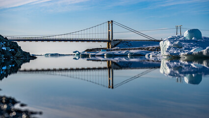 Brücke bei Jökulsarlon spiegelt sich im Wasser der Gletscherlagune, Eisschollen treiben in Richtung Meer