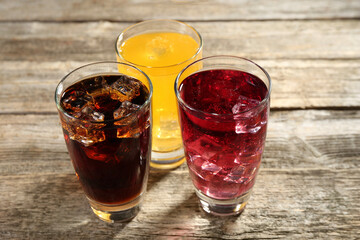 Soda water of different flavors with ice cubes in glasses on wooden table, closeup