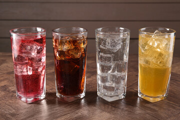 Refreshing soda water of different flavors with ice cubes in glasses on wooden table