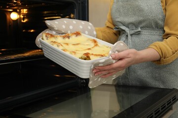 Woman taking baking dish with tasty lasagna out of oven, closeup