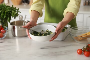 Woman making spinach lasagna at marble table indoors, closeup