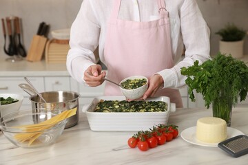 Woman making spinach lasagna at marble table in kitchen, closeup