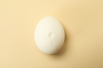 One egg with cracked shell on beige background, top view