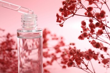 Dripping serum from pipette into bottle and gypsophila flowers on pink background, closeup