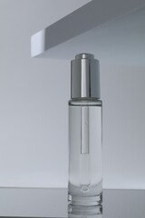 Bottle of serum on mirror surface against grey background, closeup