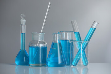 Laboratory glassware with blue liquid on mirror surface against grey background