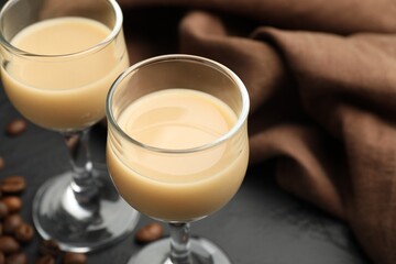 Coffee cream liqueur in glasses and beans on black table, closeup. Space for text