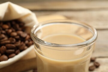 Coffee cream liqueur in glass and beans on table, closeup