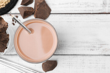 Tasty chocolate milk in glass and pieces of chocolate on white wooden table, flat lay. Space for text