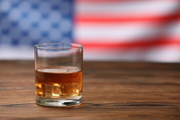 Glass of whiskey on wooden table against American flag. Space for text