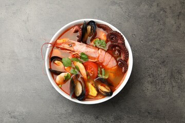 Delicious seafood soup in bowl on gray textured table, top view