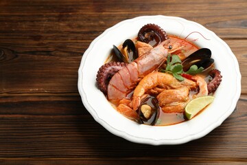 Delicious seafood soup in bowl on wooden table, closeup. Space for text