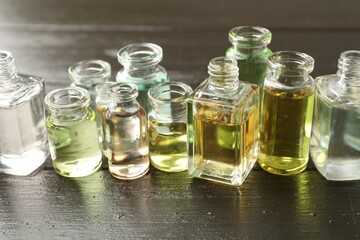 Perfume bottles with aromatic oils on black wooden background, closeup