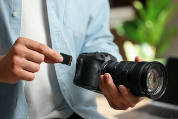 Man inserting SD memory card into photo camera indoors, closeup