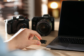 Man inserting SD memory card into laptop at wooden table indoors, closeup