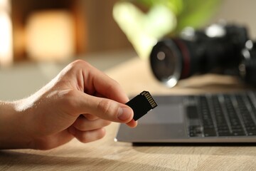 Man with SD memory card at wooden table indoors, closeup