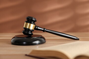 Judge's gavel, sound block and book on wooden table against coral background, selective focus