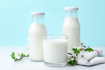 Fresh milk and blossoms on white table against light blue background