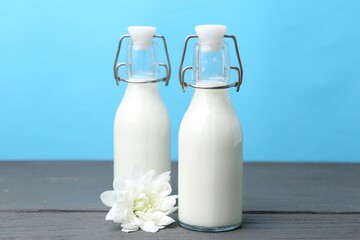 Fresh milk and flower on wooden table against light blue background