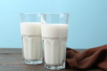 Fresh milk on wooden table against light blue background