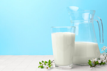 Fresh milk and blossoms on white table against light blue background. Space for text