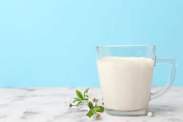 Cup of milk and blossoms on white marble table against light blue background. Space for text