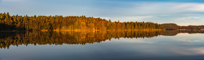 Stunning panorama of still lake reflecting autumn trees at sunrise near Gothenburg