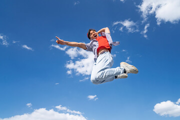 A man is jumping in the air with his arms outstretched. The sky is blue and there are clouds in the background. Scene is joyful and energetic