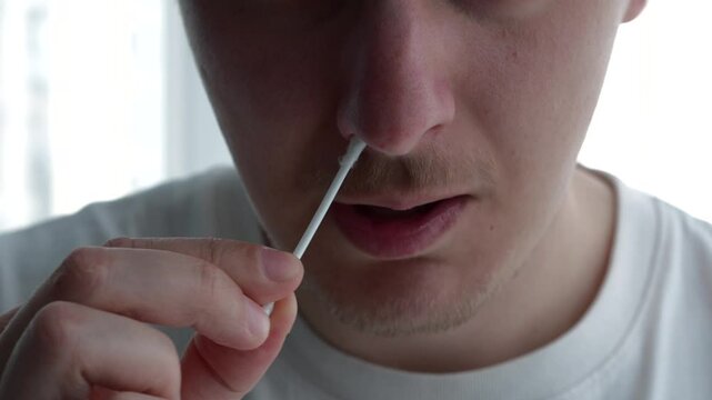 A man picks his nose with a cotton swab.
Close-up of a cotton swab in his nose.
A man in a lab taking a nasal swab test