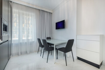 A bright kitchen with a table surrounded by four black chairs. Natural light penetrates .through the large windows, illuminating the minimalist decor and modern appliances.