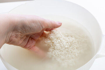 Woman's hand washing white rice in a bowl of water