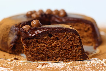 Rich, moist chocolate cake slice topped with glossy chocolate ganache and crunchy chocolate coated nuts
