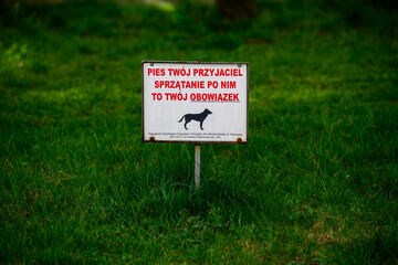 Tabliczka z napisem &bdquo;Pies tw&oacute;j przyjaciel &ndash; sprzątanie po nim to tw&oacute;j obowiązek&rdquo; na trawniku