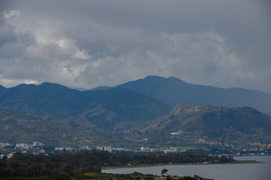 Majestic mountain ranges loom over a tranquil coastal town under a dramatic cloudy sky at dusk