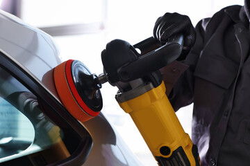 Obraz premium Man polishing car with orbital polisher indoors, closeup