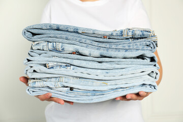 Woman with stack of different stylish jeans near light wall indoors, closeup
