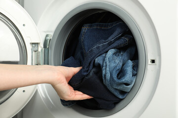 Woman putting jeans into washing machine, closeup