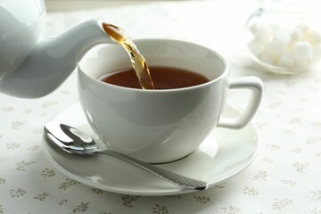 Pouring aromatic tea into cup from teapot at table, closeup