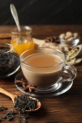 Aromatic Masala tea in cup, spices, dry leaves and honey on wooden table, closeup
