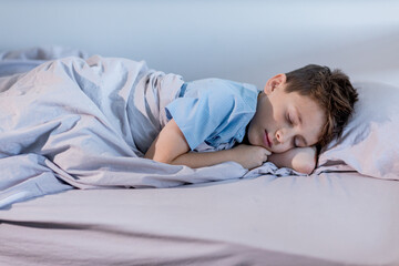 A young boy wearing a blue shirt is peacefully sleeping on his cozy bed tucked in with soft...