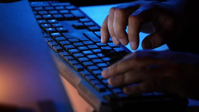 Hands typing on a computer keyboard at night. Internet safety. Working on a computer late at night. Writing replies or comments. Black keyboard and hands with soft lighting. Cybercrime.