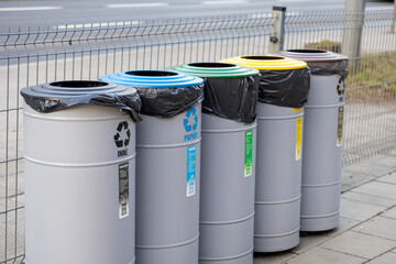 Row of colorful recycling bins for paper, plastic, metal, glass and mixed waste on city sidewalk, promoting organized waste separation and environmental awareness