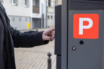 Man pressing button on parking meter in city street, close-up of hand interacting with urban...