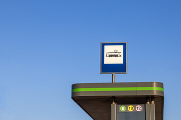 Tram stop sign on top of modern shelter against clear blue sky with line numbers visible and no...