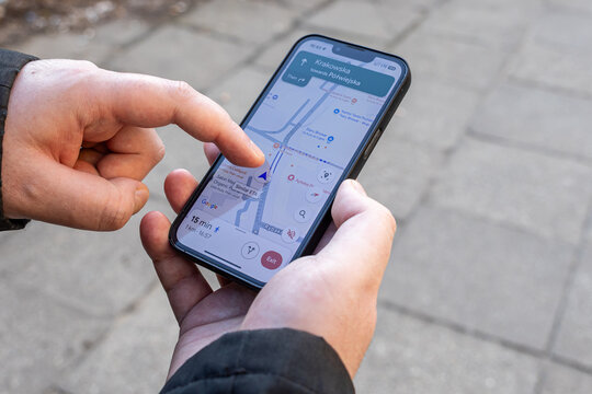 Poznan, Poland - March 15, 2025: man using smartphone navigation app with google maps directions on screen while standing on sidewalk and searching walking route to destination in urban area