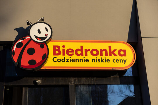 Poznan, Poland - March 15, 2025: biedronka store sign with smiling ladybug logo and daily low prices slogan on bright yellow background in sunlight outside modern supermarket entrance