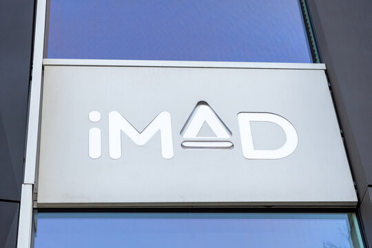Poznan, Poland - March 15, 2025: imad store logo on modern glass building facade with silver metallic sign and clean minimalist design reflecting blue sky in urban city environment