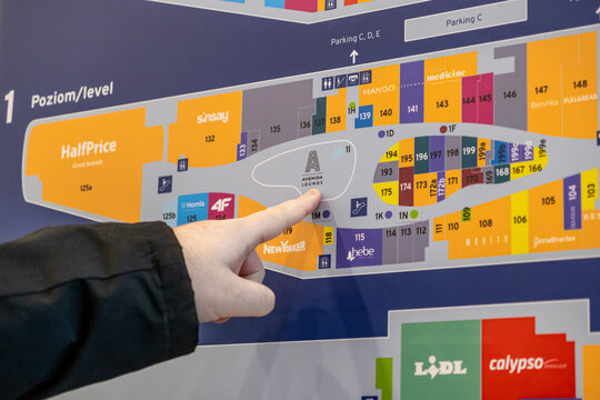 Poznan, Poland - March 15, 2025: Person pointing at shopping mall directory map with visible store names and color-coded layout of Avenida Poznań level one, showing retail zones and amenities